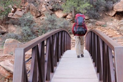 man_with_hiking_backpack_walking_across_bridge_596282